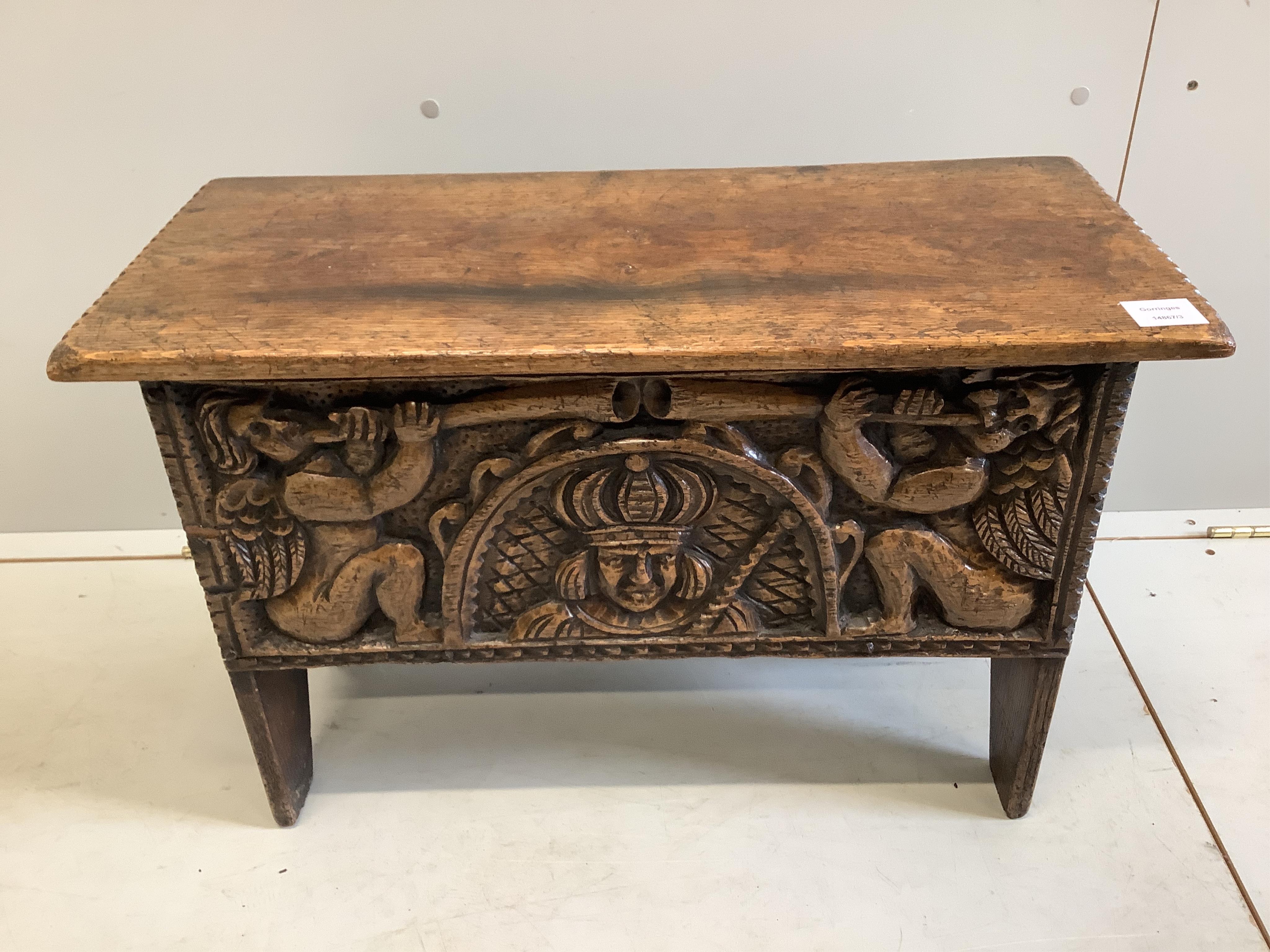 A small reproduction Tudor style carved oak coffer, the front carved with a king and trumpeting cherubs, width 68cm, depth 31cm, height 45cm. Condition - good